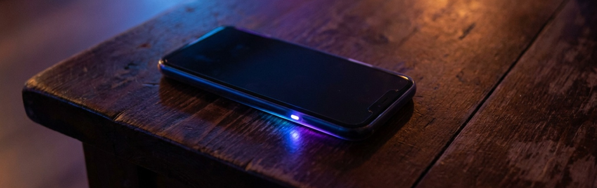 Close-up van een smartphone die in het donker op een tafel ligt, met het scherm oplichtend door binnenkomende berichten