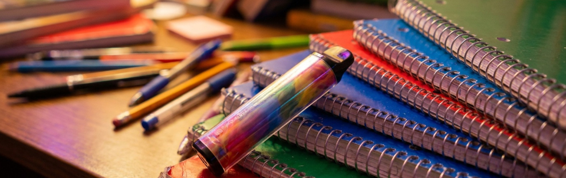 Close-up van een kleurrijke wegwerp-vape die bovenop een stapel schoolboeken op een bureau ligt