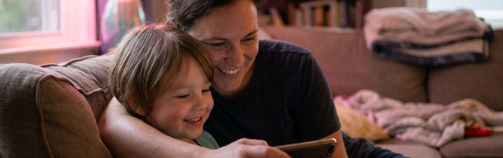 Close-up van een ouder en kind die samen glimlachend naar een smartphone kijken