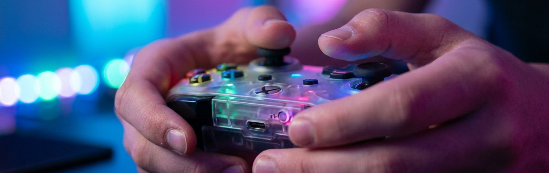 Close-up van de handen van een tiener die een kleurrijke game-controller vasthoudt, met zachte gekleurde gaming-verlichting op de achtergrond