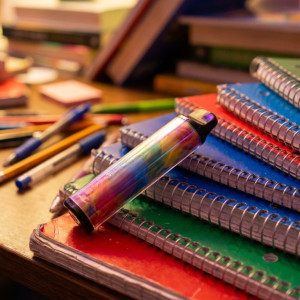 Close-up van een kleurrijke wegwerp-vape die bovenop een stapel schoolboeken op een bureau ligt
