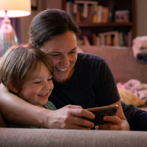Close-up van een ouder en kind die samen glimlachend naar een smartphone kijken