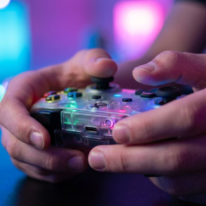 Close-up van de handen van een tiener die een kleurrijke game-controller vasthoudt, met zachte gekleurde gaming-verlichting op de achtergrond